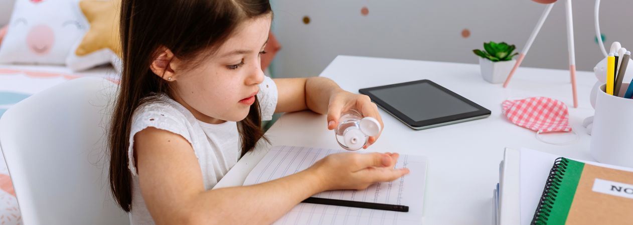 Girl applying hand sanitizer while doing homework
