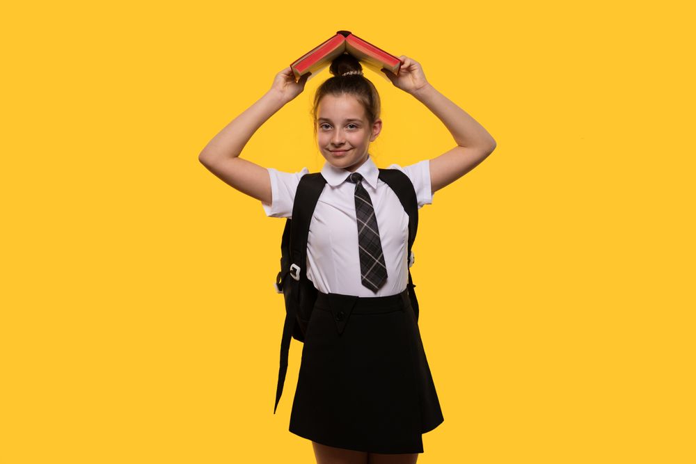 Teen girl holding book over head, wearing school uniform