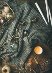 Festive decorations, candles and garland resting on grey woolen sweater