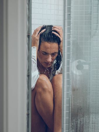 Depressed woman sitting on shower cabin and touching head