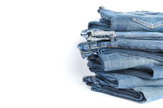 Stack of blue jeans on light background, space for text