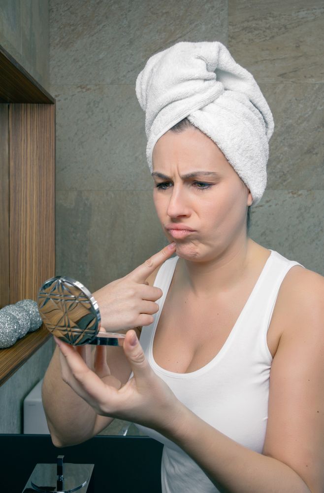 Unhappy woman looking an acne pimple in mirror