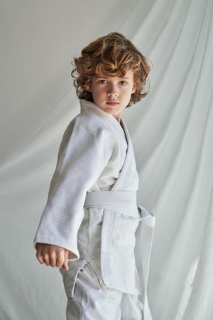 Unemotional curly haired boy in kimono near white curtain