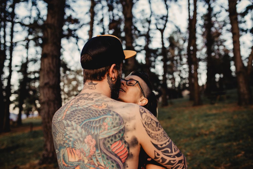 Young guy in tattoos hugging woman in forest