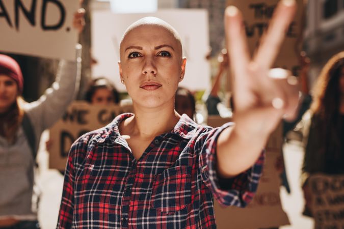 Bald woman protesting outdoors and showing a peace hand sign