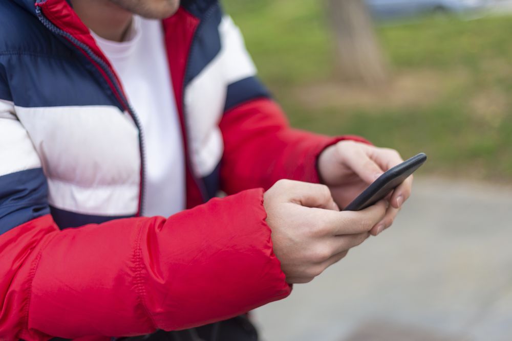 Young man with smartphone in hand texting outdoors in the street