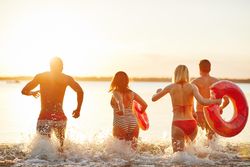 Multi-ethnic group of friends walking into the water at sunset