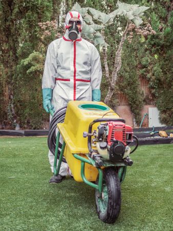 Specialist in uniform for fumigation holding yellow trolley in yard