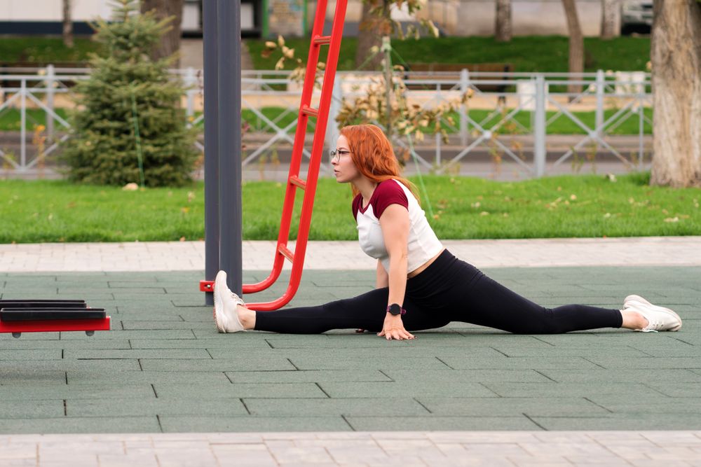 Woman doing the splits on outdoor fitness equipment