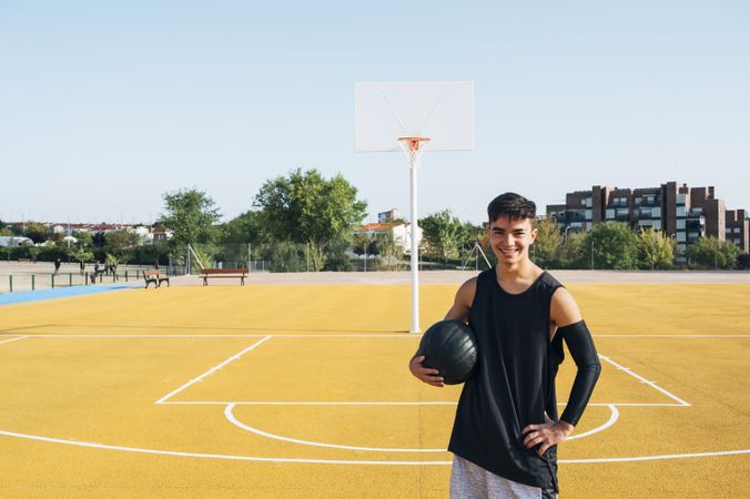 Young man playing on yellow basketball court outdoor.