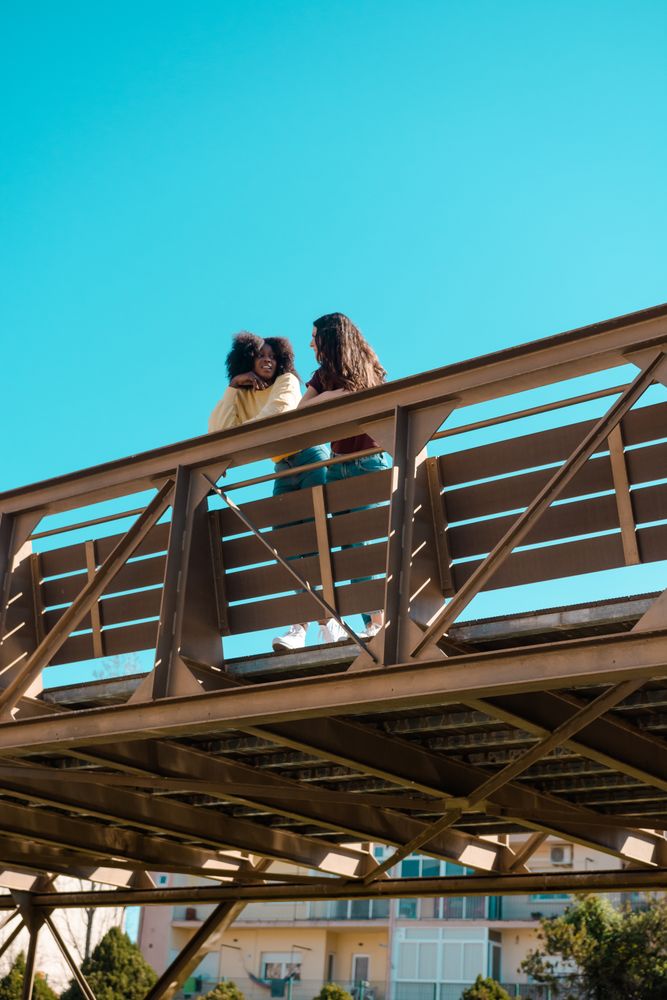 Two female friends talking on a bridge.