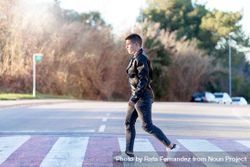 Side view of teenage male wearing a leather jacket walking on crosswalk 4AYpR4