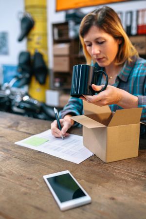 Woman preparing new merchandise to sell in local store. Parcel delivery and ecommerce concept.