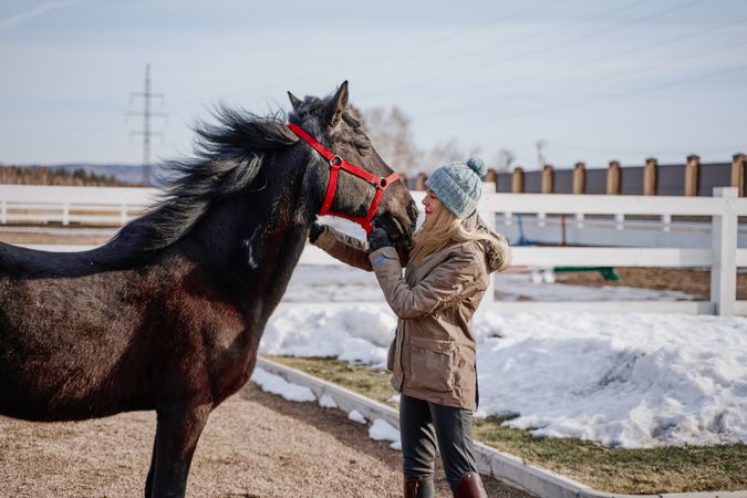Warm dressed woman with brown horse by hay