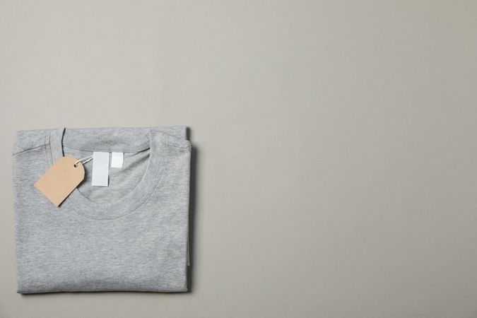 Folded blank gray t-shirt with tag on gray background, space for text