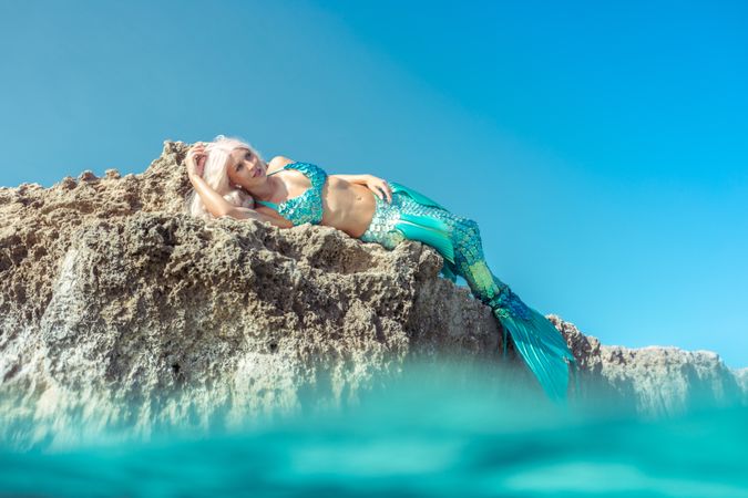 Blond fairytale female mermaid lying on rock