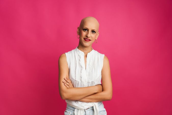 portrait of a woman with cancer with hairless head and crossed arms on pink background