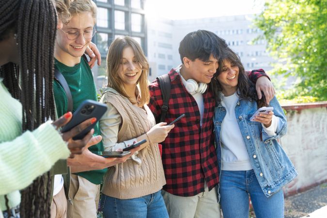 Smiling multi-ethnic group of students hanging out on campus using their phones