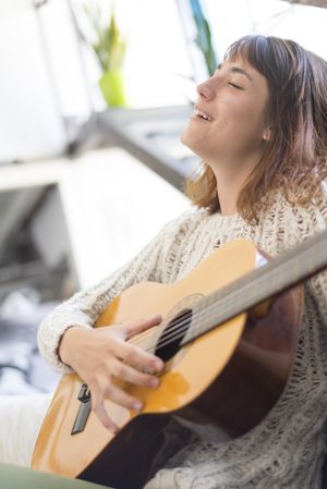 Female with head back in wool sweater strumming acoustic guitar