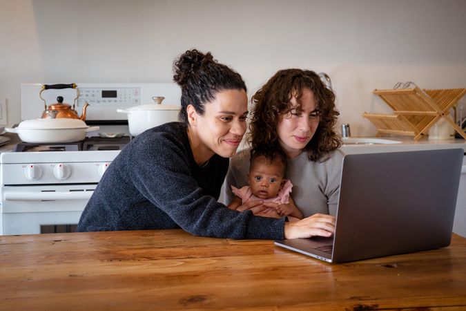 Two women working on video chat at kitchen table with baby