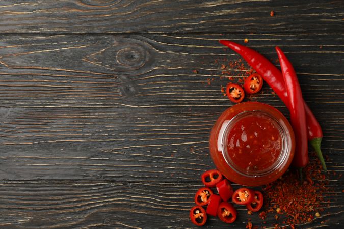 Chilli pepper and glass jar of sauce on wooden  background, top view