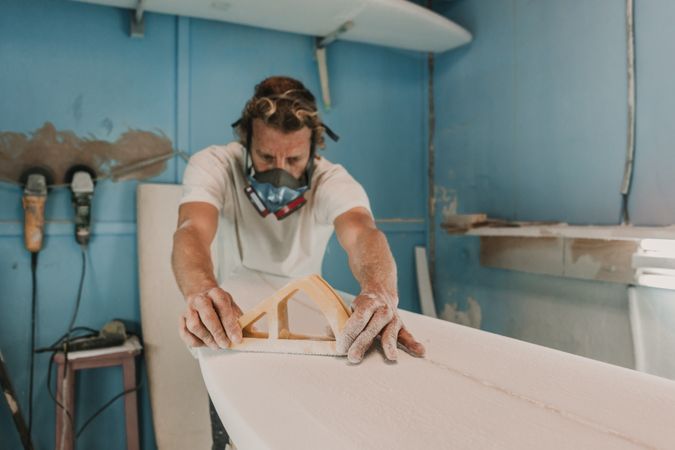 Man in respirator polishing surf board in workshop