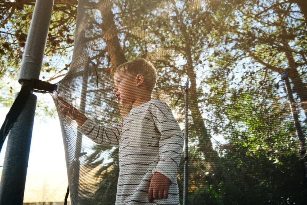 Boy standing and touching trampoline net in park
