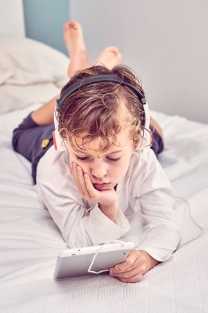 Boy lying on bed and watching video on tablet