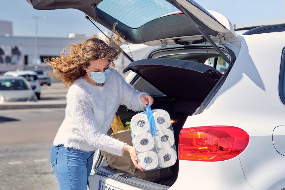 Young woman in mask placing purchases in car trunk
