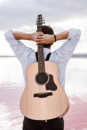 Musician gazing and carrying guitar behind back while standing on beach