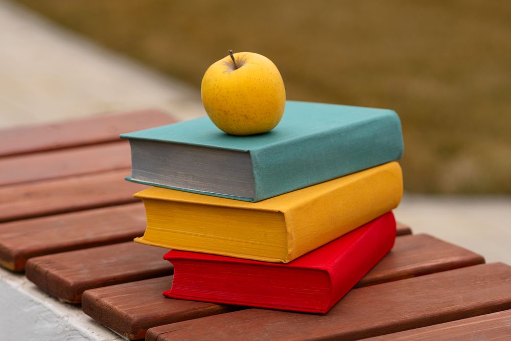 Yellow apple placed on stack of three colorful books.