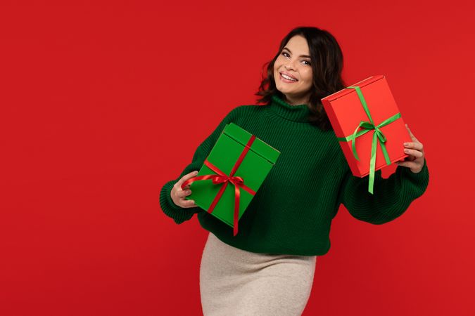 Woman in green sweater joyfully holding two wrapped gift boxes