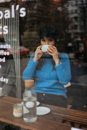 stylish woman drinking coffee into a coffee shop looking away