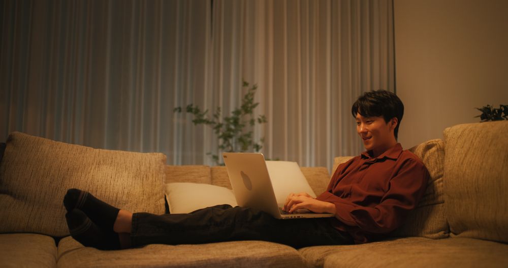 South Korean Man Resting on a Sofa at Home, Using Laptop Computer