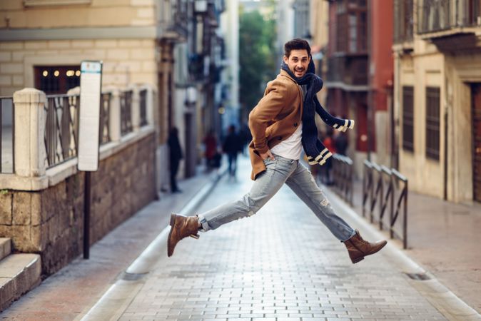 Handsome man in scarf leaping in center of street