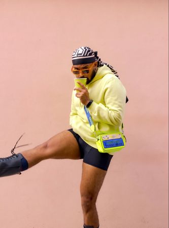 South Asian wearing bandana and eyeglasses holding a plastic cup and kicking one leg