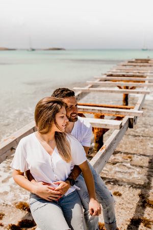 Glad lovers sitting on destroyed pier on seashore