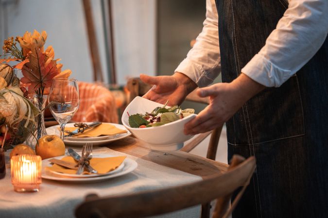 Cropped image of a waiter putting a bowl of salad on dinner table