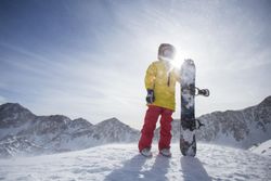 Portrait of man standing next to snowboard on mountain top
