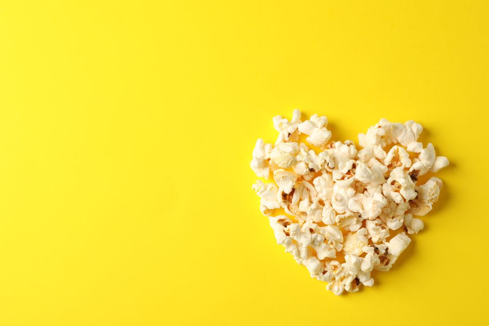 Flat lay composition with popcorn heart on yellow background, space for text