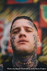 Man with face and neck tattoos and nose ring against colorful blurred background bE9wob