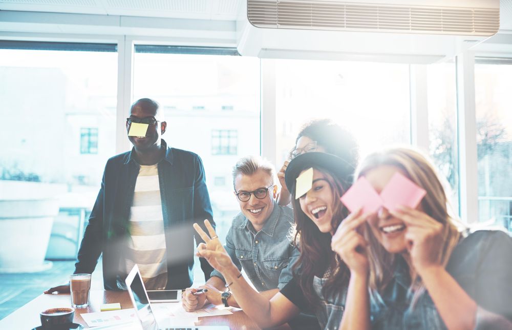 Multi-ethnic group of people smiling while joking around with sticky notes
