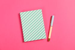 Copybook and pen on pink background, space for text