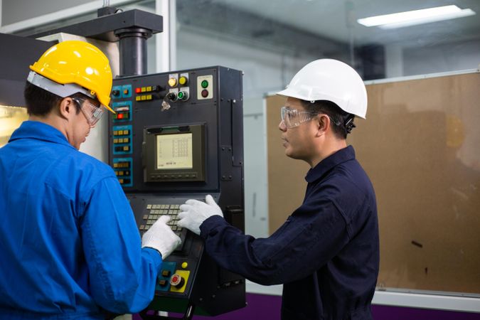 Two men in PPE gear operating controller in factory
