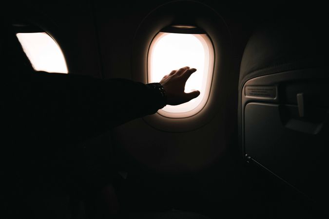 Person reaching out hand toward airplane window