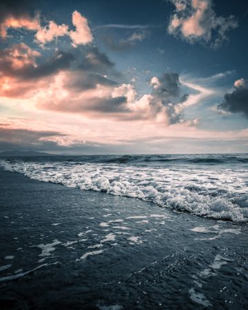 Waves of sea crashing on shore during cloudy sunset
