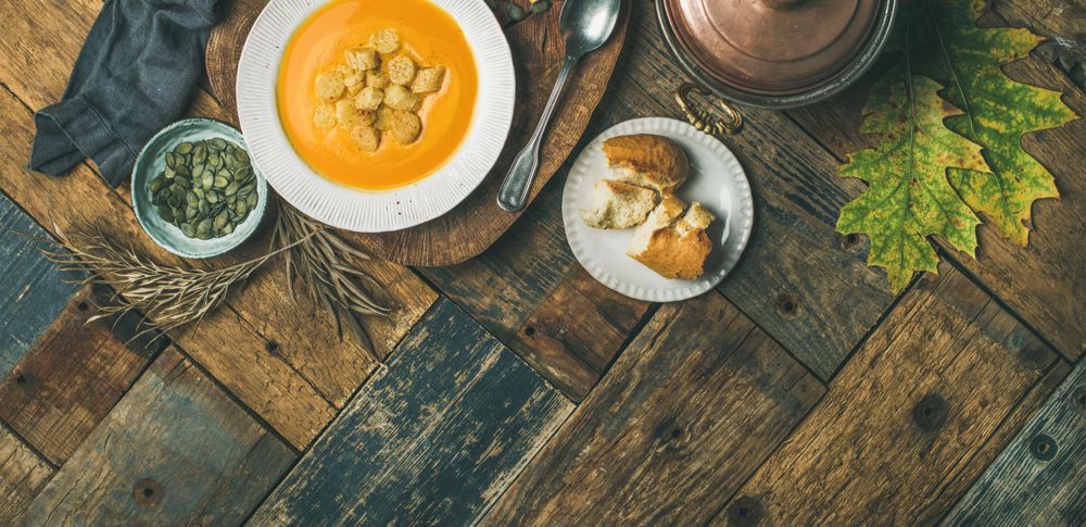 Pumpkin soup with croutons, bread, seeds, pot, spoon on wooden table, wide composition, copy space
