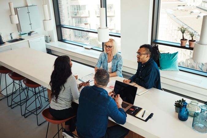 Group of colleagues having a laid back meeting near the kitchen in a bright modern office