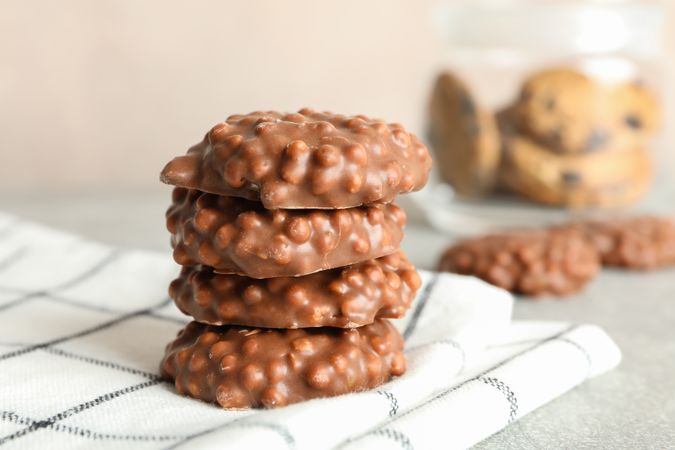 Stack of chocolate cookies on kitchen towel against light background, space for text