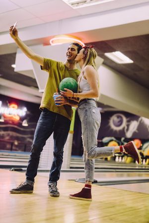 Smiling couple with bowling balls taking self portrait using smartphone